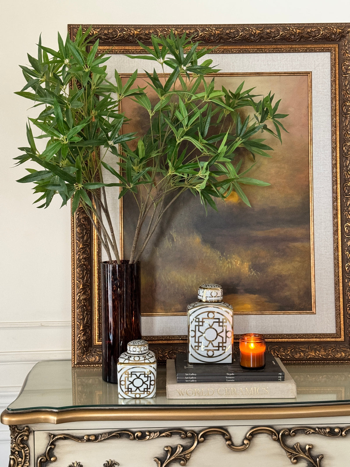 White and gold lattice lidded jars, tortoiseshell vase with faux bamboo stems and a gilded landscape painting on a console – Bohemia Lifestyle