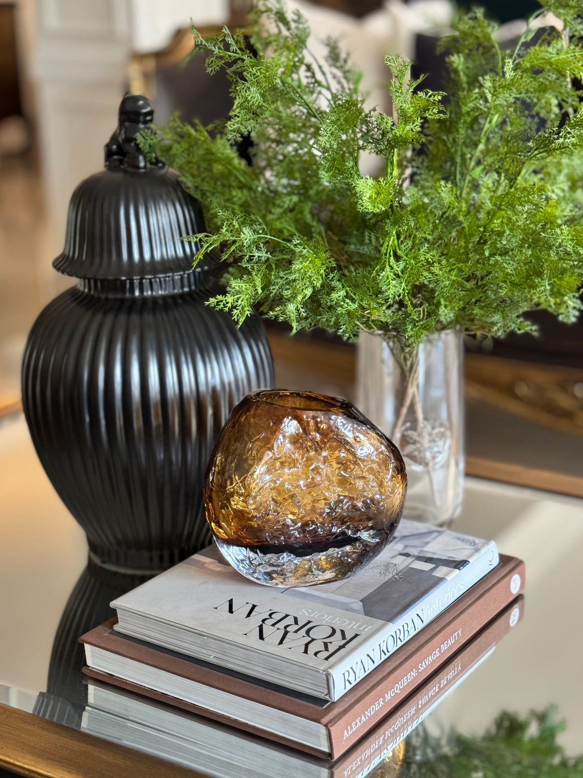 The Amber Boulder Vase on a stack of design books, with Feathered Cedar Spray in a glass vase and the Noir Dynasty Temple Jar